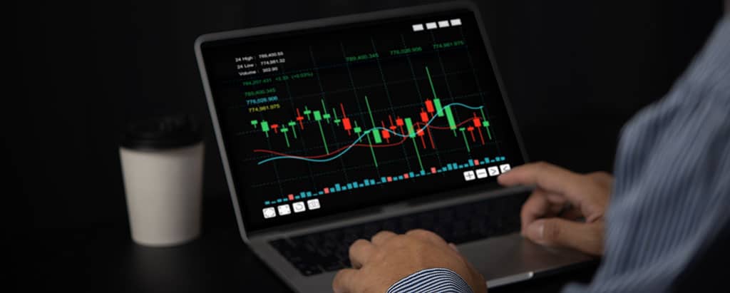 Person using a laptop that shows a stock market chart with red and green candlesticks and moving averages.